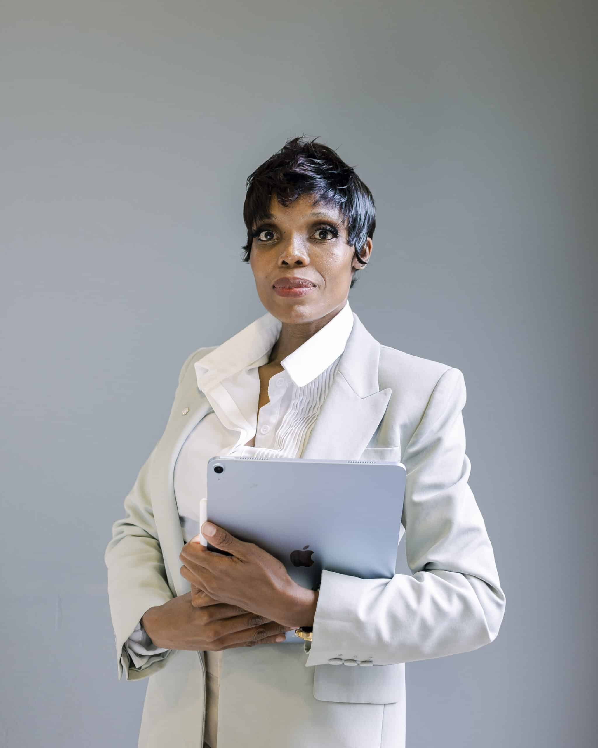 Fotoshooting für Gründer – Ann Sophie Detje – Personal Branding Fotografin: Eine Frau in hellem Business-Anzug und weißer Bluse steht vor neutralem Hintergrund. Sie hält ein Tablet im Arm und blickt selbstbewusst in die Kamera.